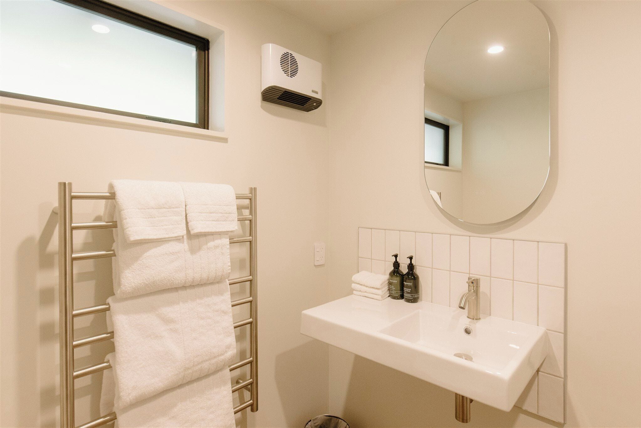 A bathroom with a towel rack, a sink, a mirror, and an air conditioning unit.
