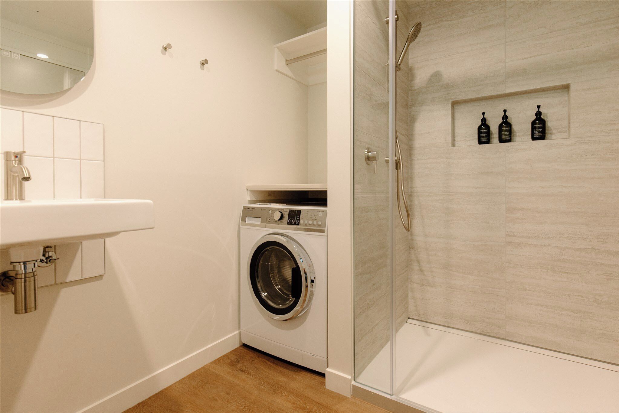 A compact bathroom with a washing machine, a sink, and a glass-enclosed shower.