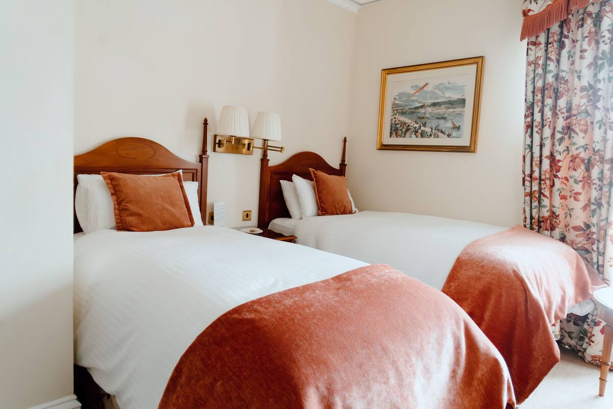 A hotel room with two beds, a nightstand, a lamp, and a framed picture on the wall.