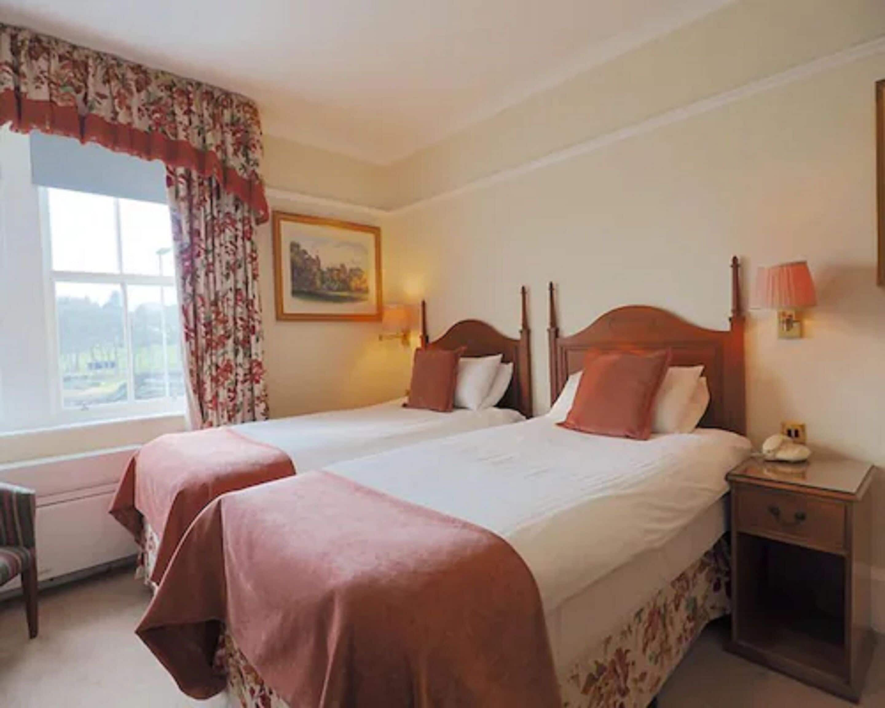 A double bed with a wooden headboard, a nightstand with a lamp, and a window with floral curtains.