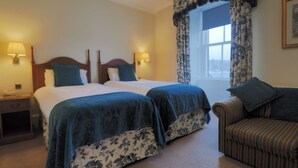 A hotel room with two beds, a sofa, and a window with floral curtains. - The Royal Hotel (Stornoway)