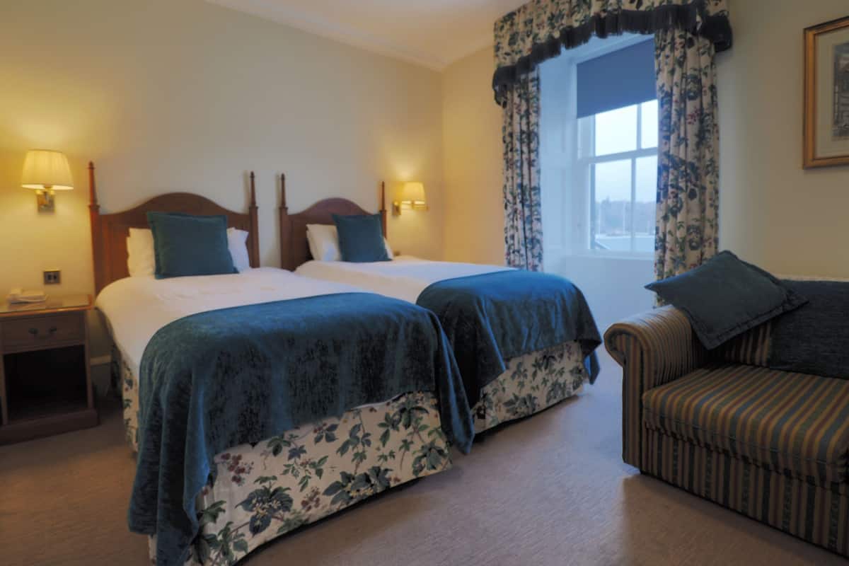 A hotel room with two beds, a sofa, and a window with floral curtains.