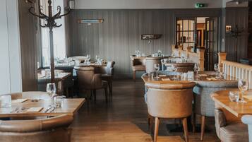 A restaurant with wooden tables and chairs, a high ceiling, and a view through an open door.