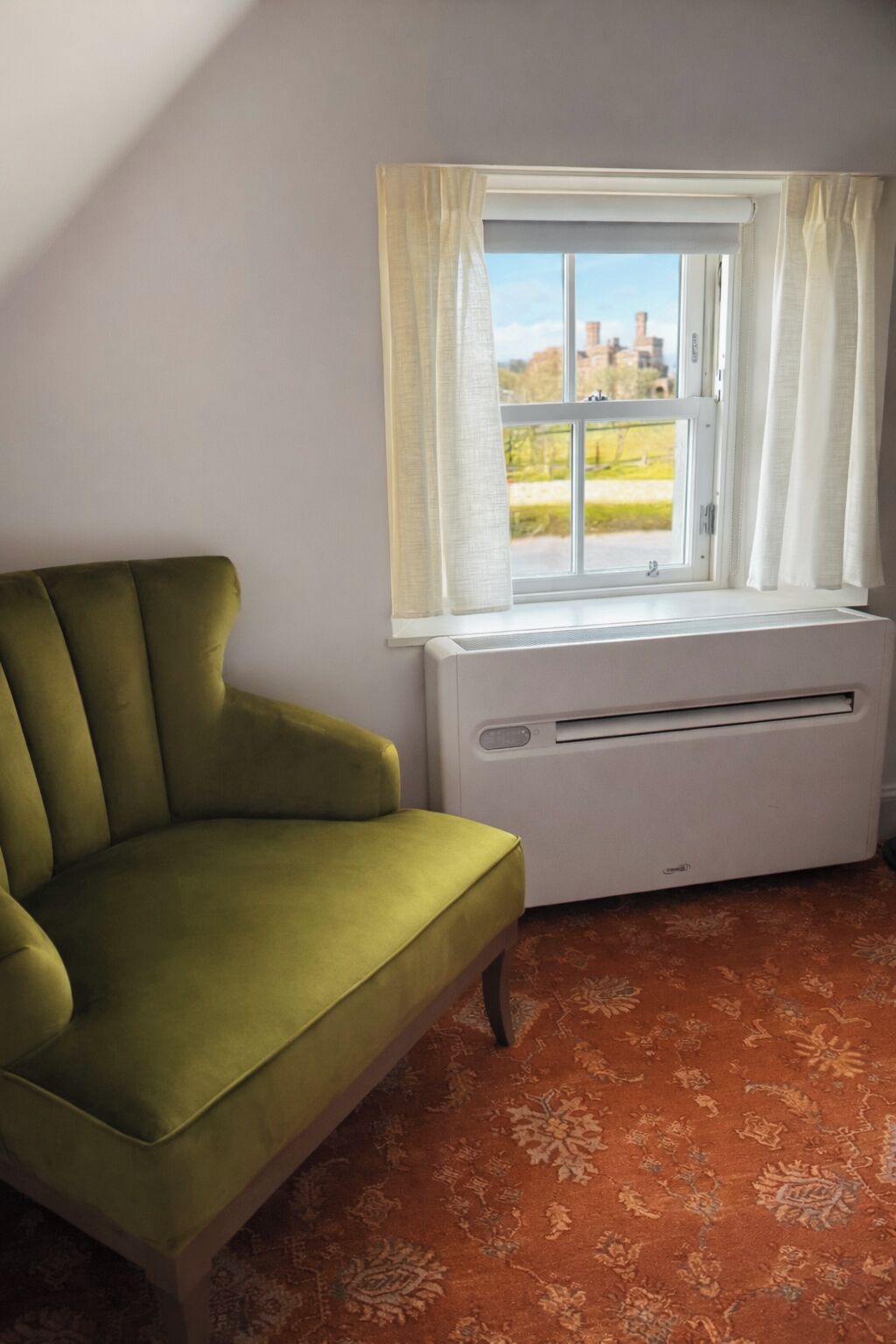 A room with a green armchair, a window with white curtains, and a radiator.