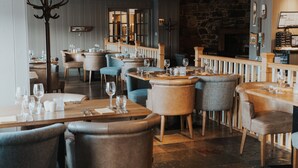 A restaurant interior with wooden tables and chairs, a stone wall, and a bar area. - The Royal Hotel (Stornoway)