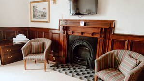 A room with a fireplace, two striped armchairs, a television, and a framed picture on the wall. - The Royal Hotel (Stornoway)