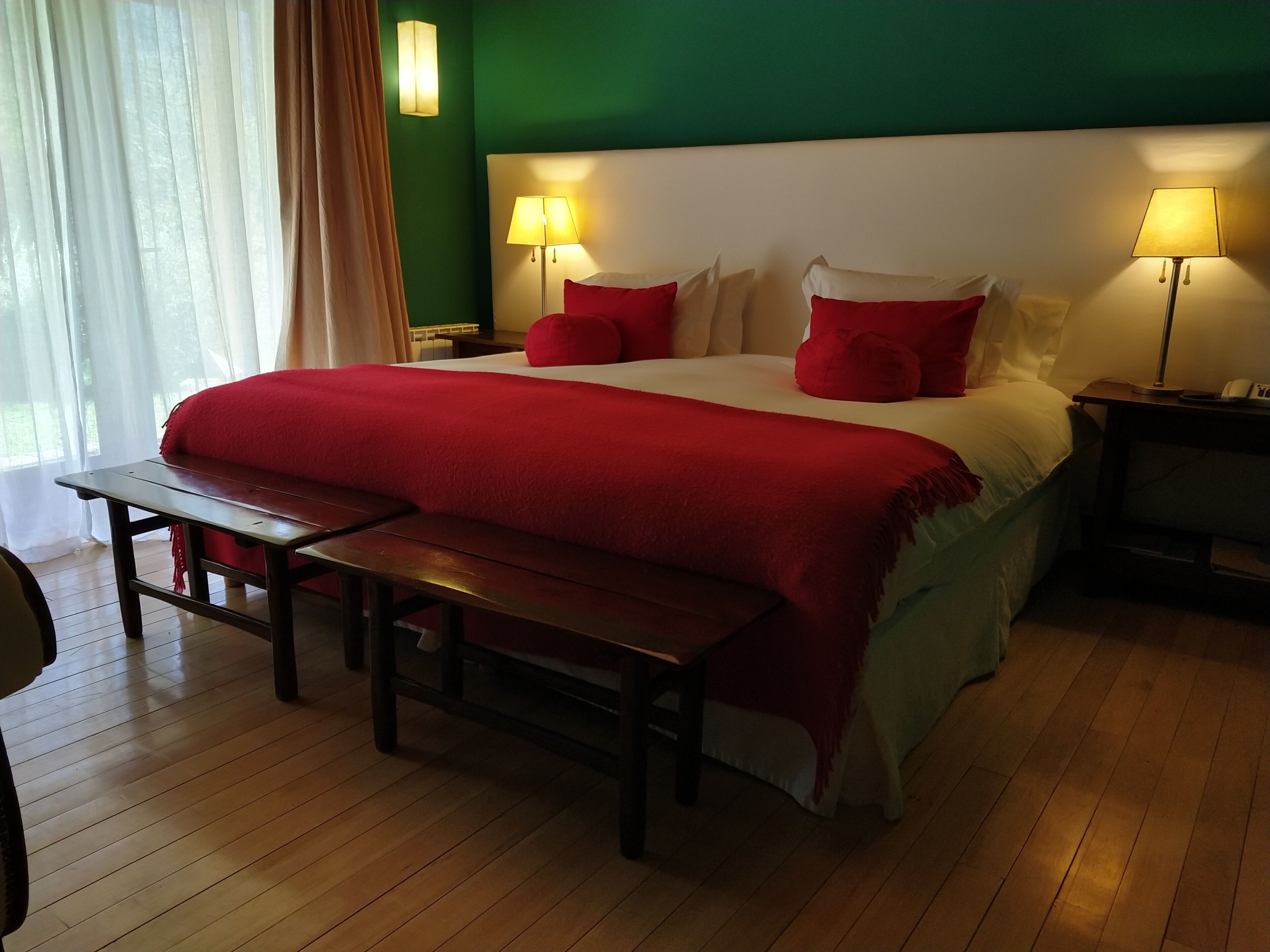 Une chambre d’hôtel bien aménagée, avec un grand lit, deux lampes de chevet, un banc et une table de chevet.