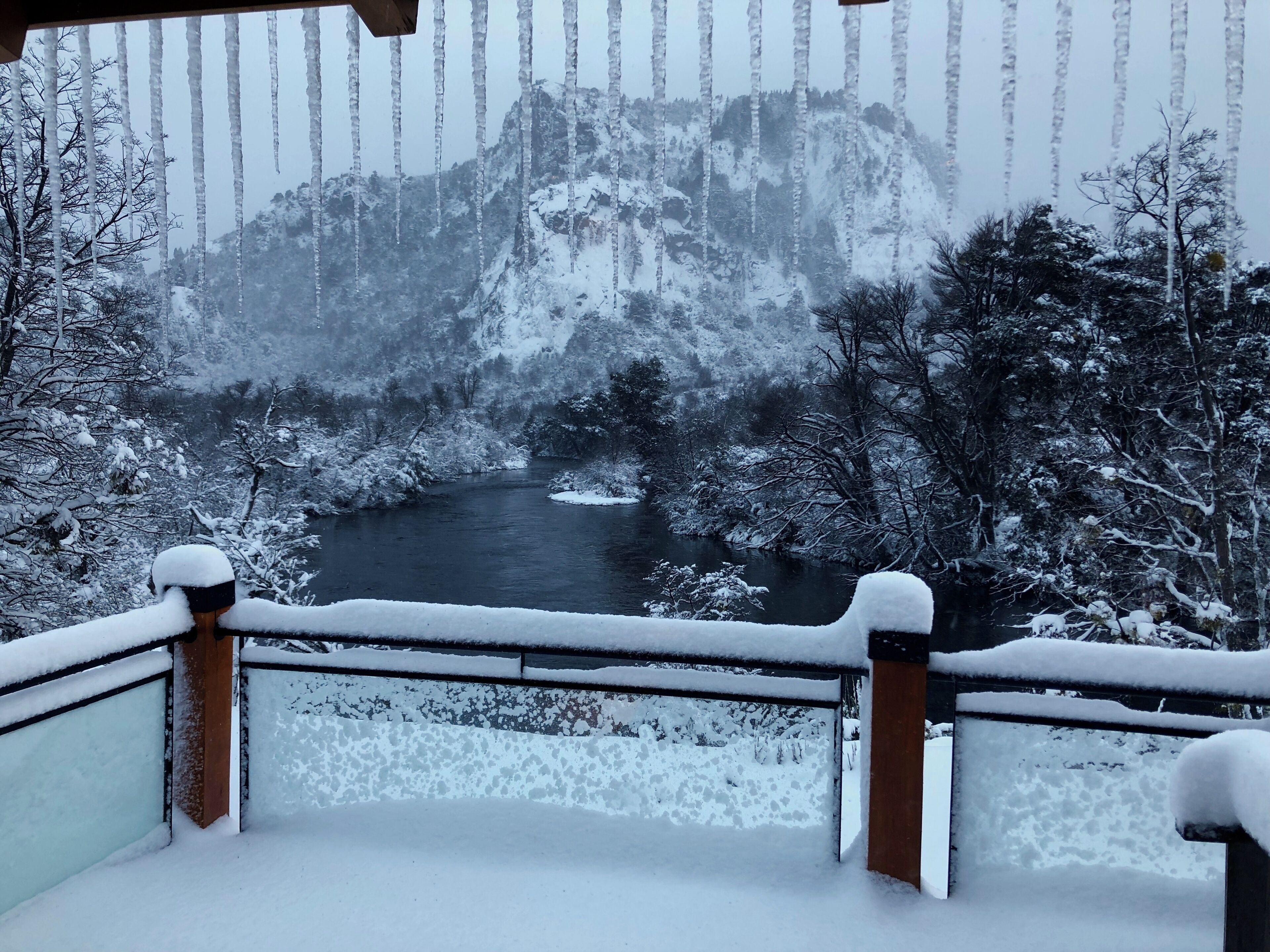A snow-covered balcony with a view of a river and mountains.