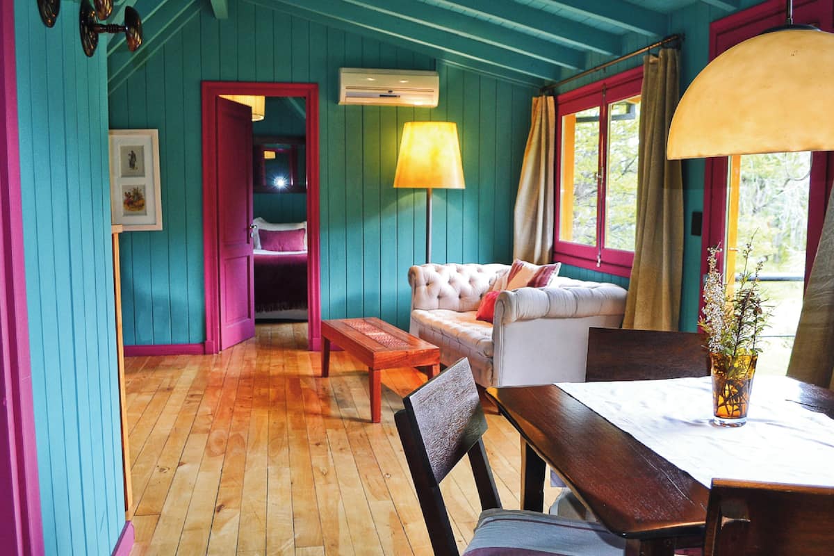 A room with teal walls, a wooden floor, a white sofa with red cushions, a wooden table, and a lamp.