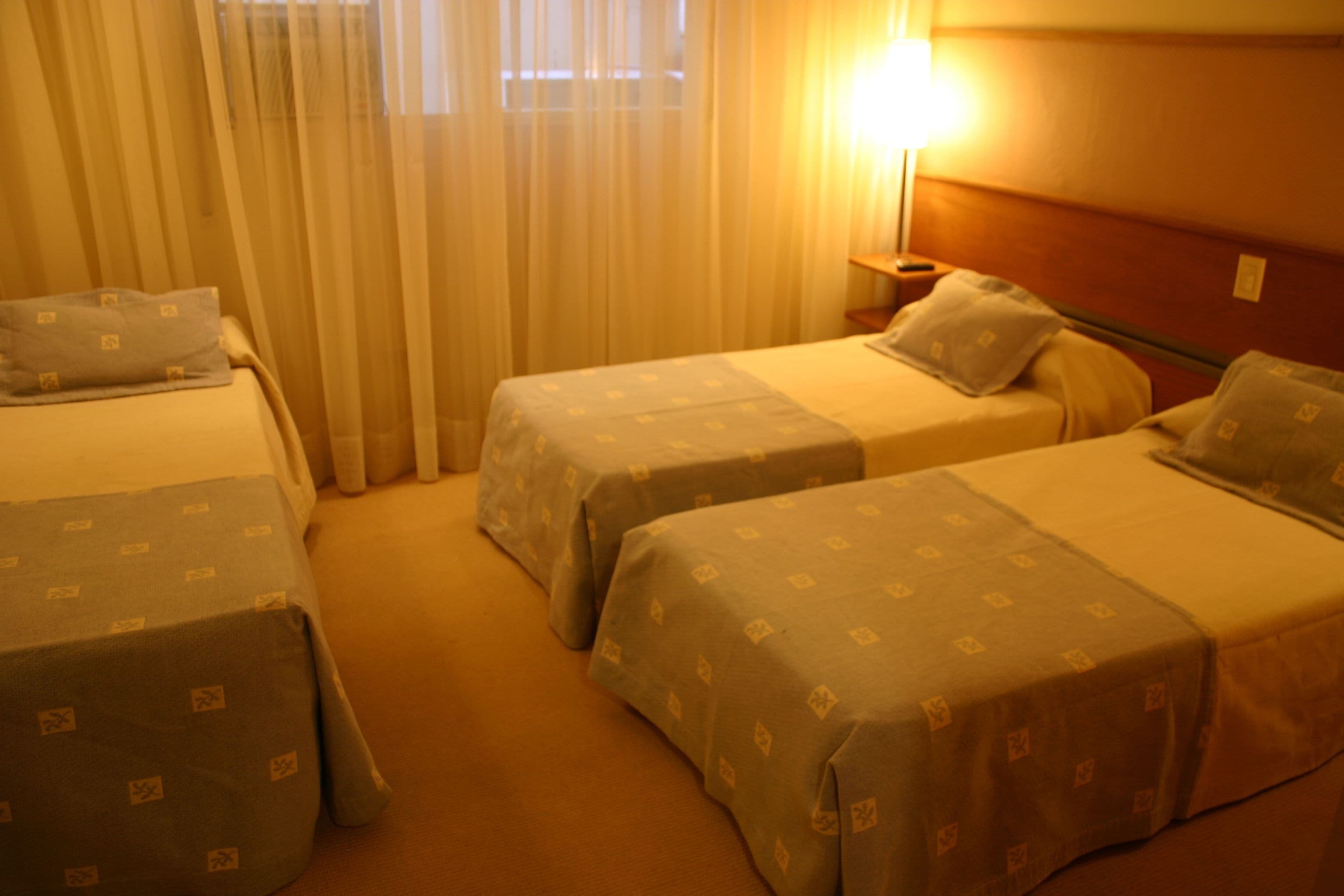 Habitación de hotel con dos camas individuales, una mesita de noche y una lámpara.