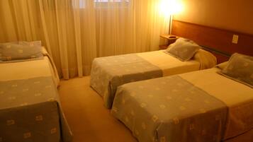 Habitación de hotel con dos camas individuales, una mesita de noche y una lámpara.