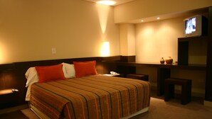 A hotel room with a large bed, a bedside table, a TV, and a small desk with a chair. - Cordon del Plata (Mendoza)