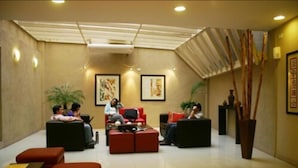 A lobby with red and black sofas, a large potted plant, and framed artwork on the walls. - Cordon del Plata (Mendoza)