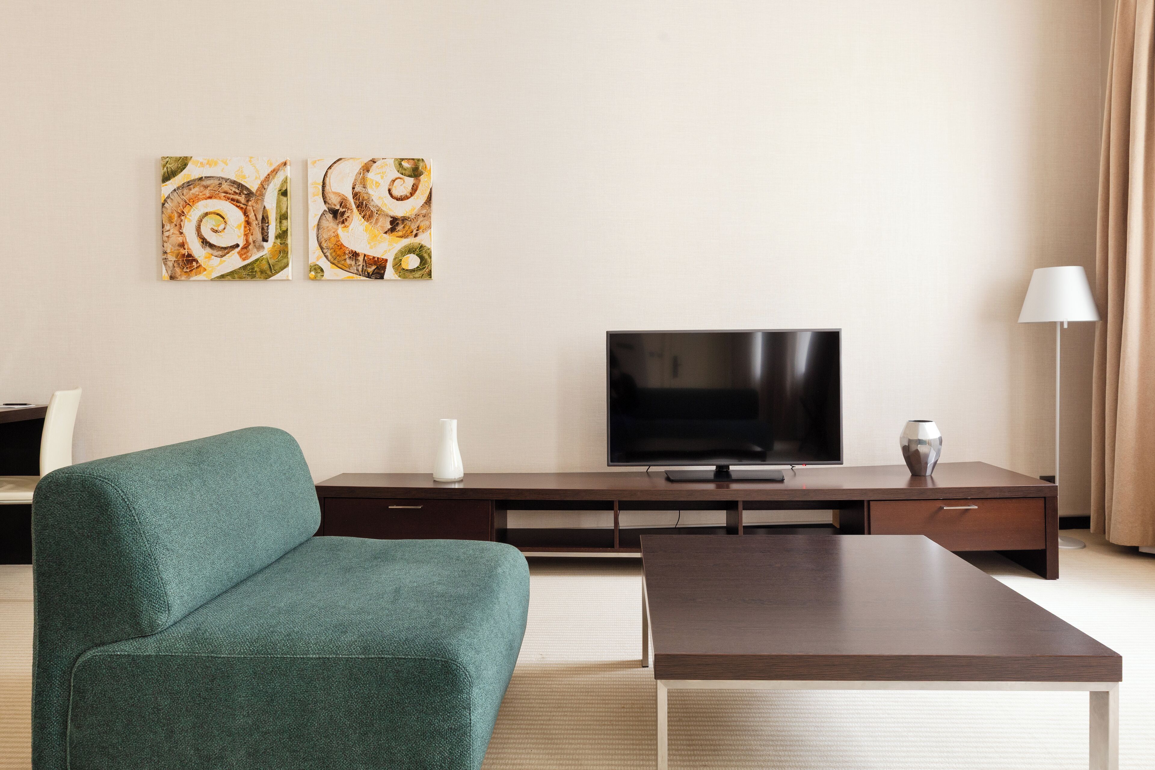 Uma sala de estar moderna com um sofá verde-água, uma TV de tela plana e duas pinturas abstratas na parede.