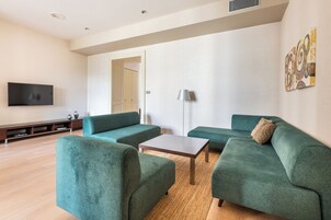 Una sala de estar moderna con un televisor de pantalla plana, sofás verdes, una mesa de centro y una lámpara.