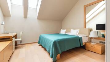 A bedroom with a bed, desk, chair, and a nightstand with a lamp.