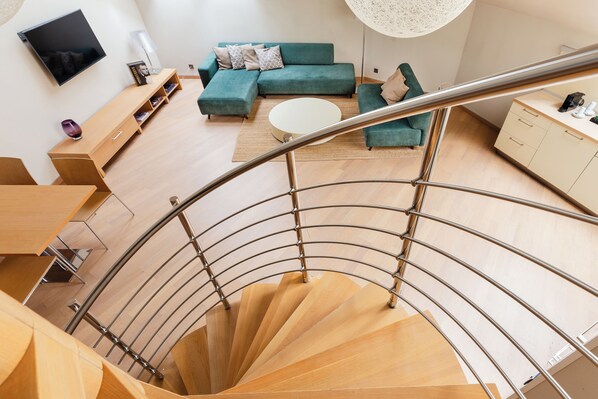A modern living room with a spiral staircase, a sectional sofa, a coffee table, and a flat-screen TV.