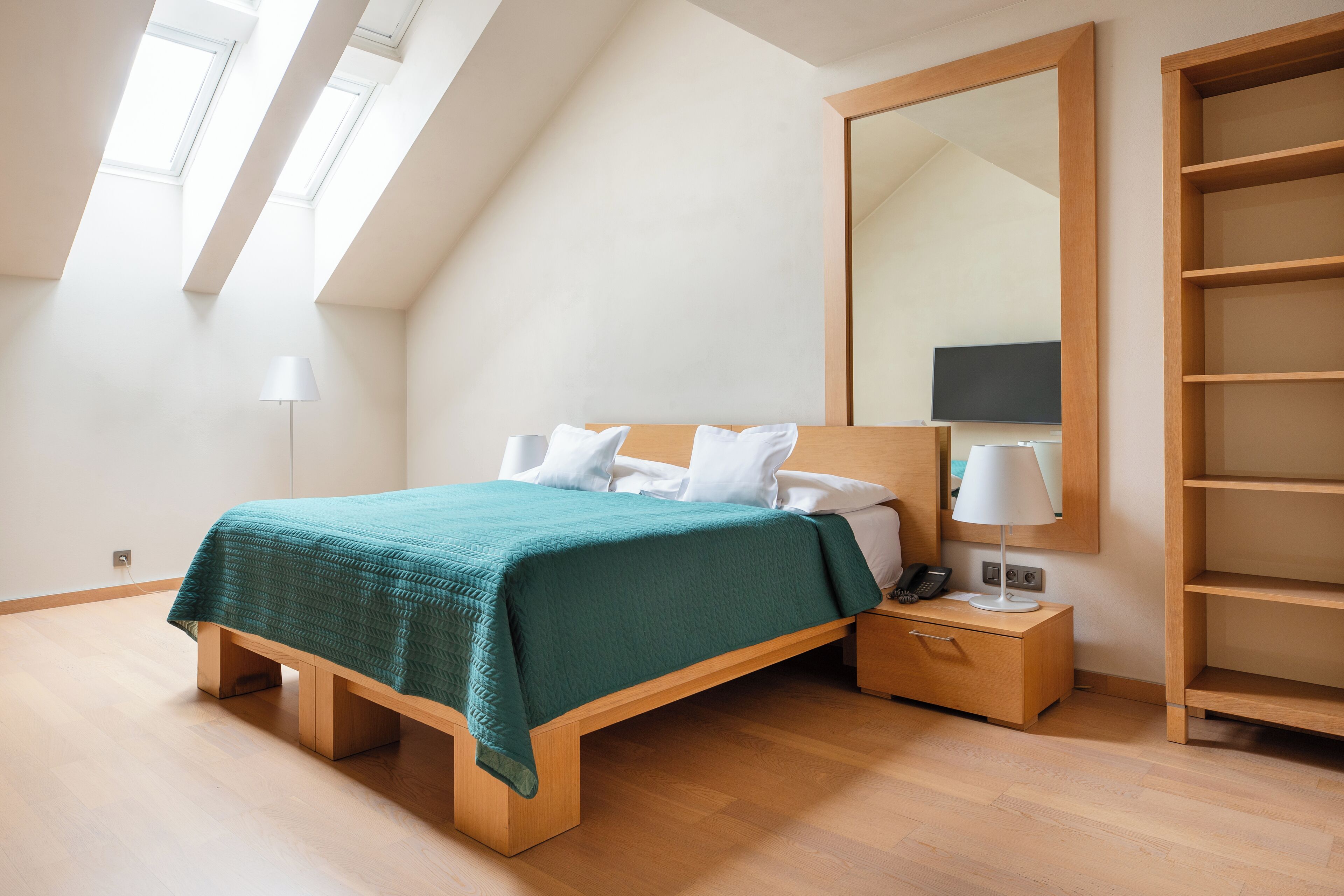 A modern bedroom with a bed, bedside tables, a mirror, and a built-in shelf.