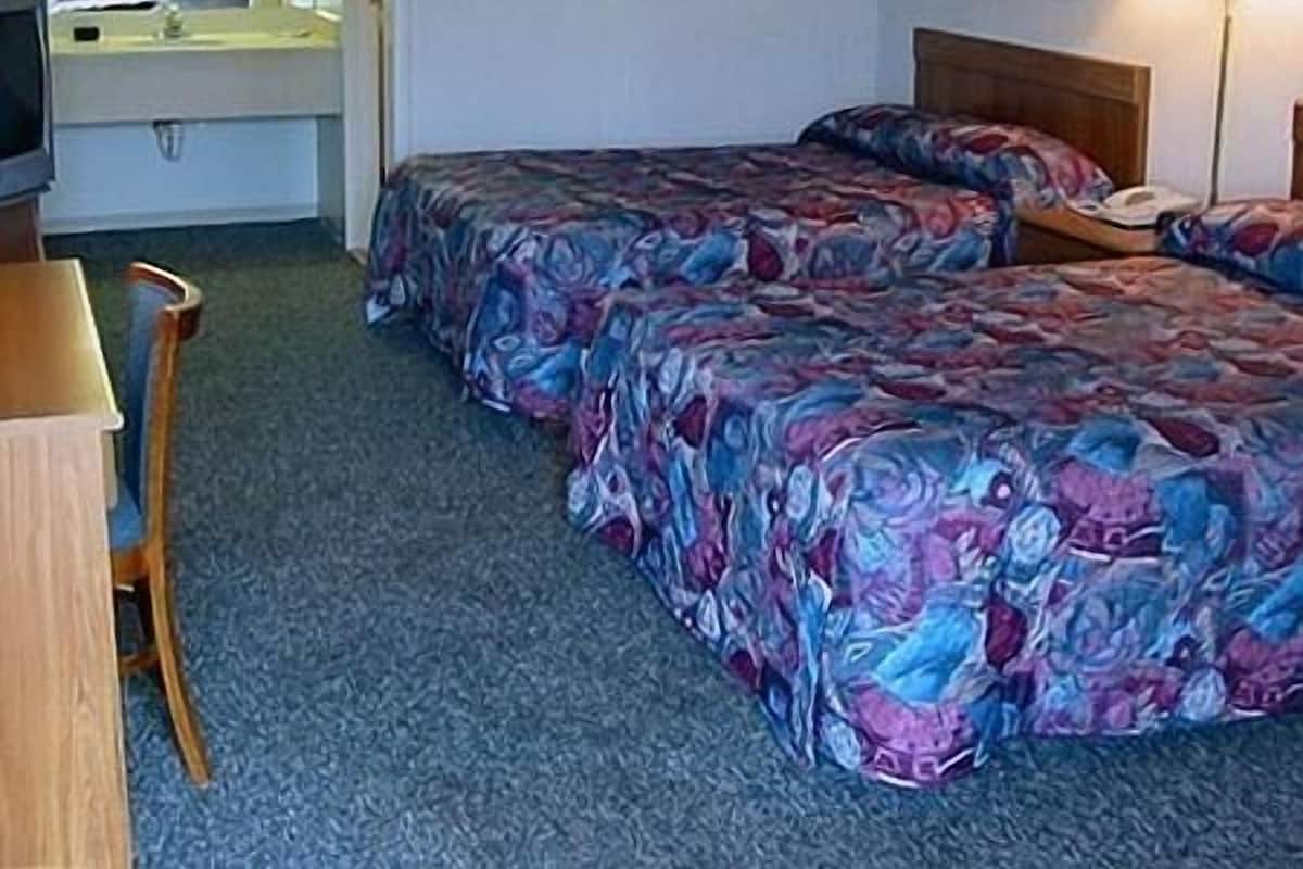 A hotel room with two beds, a desk, a chair, a television, and a bathroom visible through an open door.