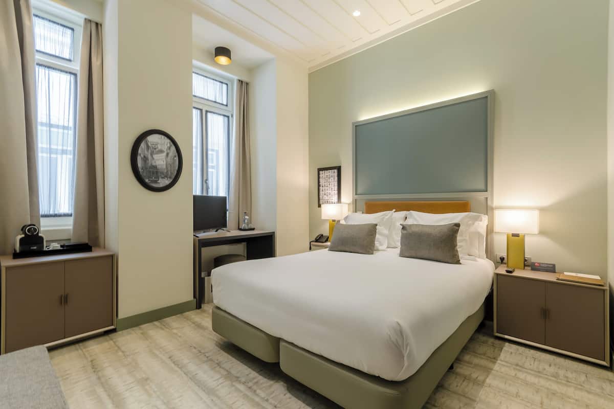 Camera d'albergo con un letto grande, comodini, una scrivania e una finestra con tende.