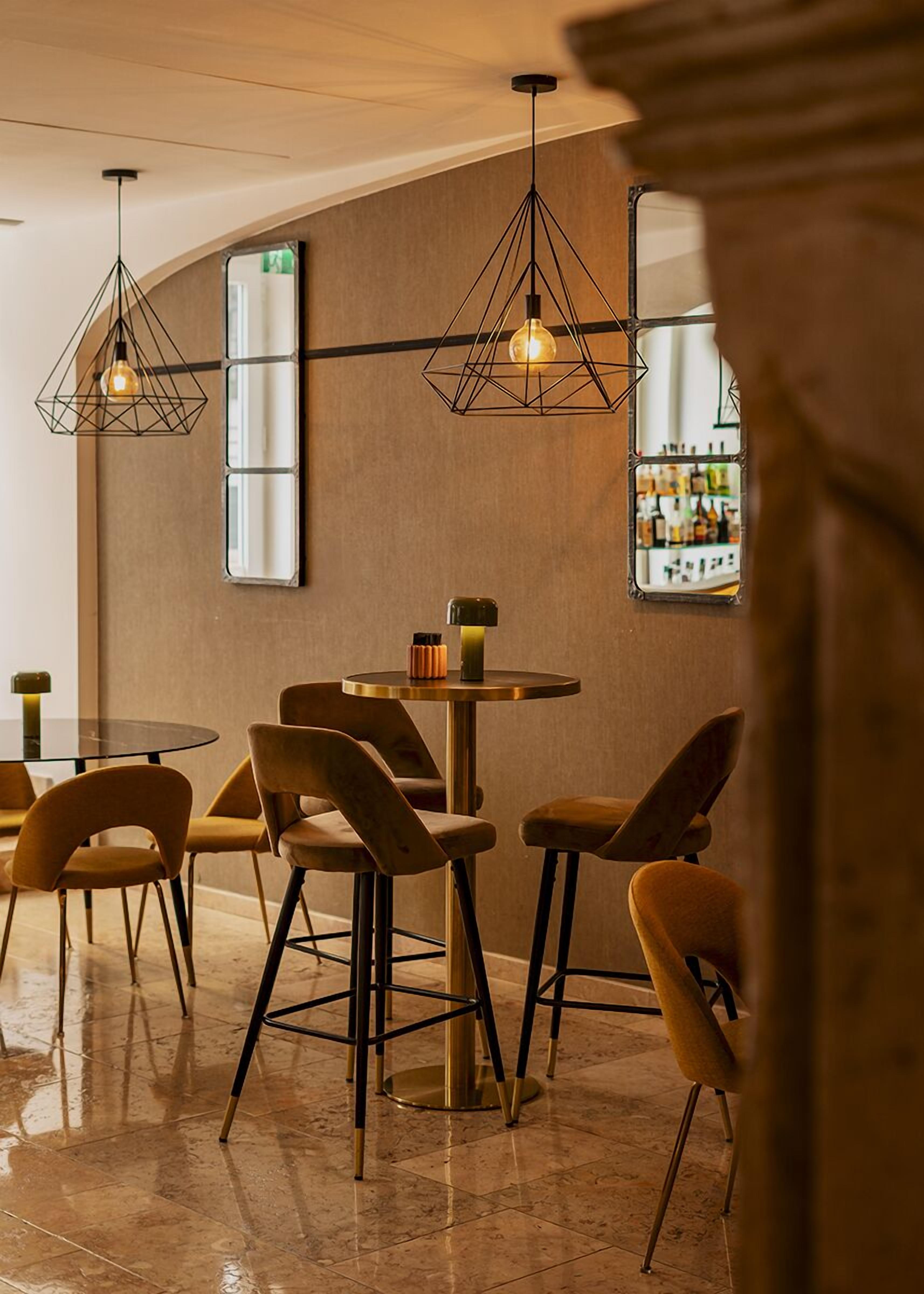 Eine moderne Bar mit runden Tischen und Stühlen, geometrischer Pendelleuchten und einer Theke voller Flaschen.