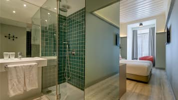 Una habitación de hotel moderna con ducha de vidrio, una cama grande, una silla roja y un televisor montado en la pared.
