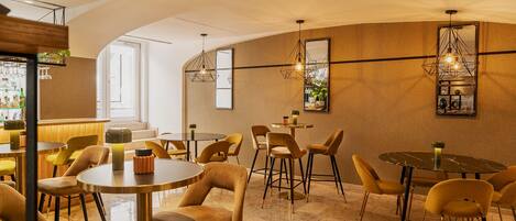 A modern interior with round tables and yellow chairs, a bar area with bottles, and decorative wall mirrors.