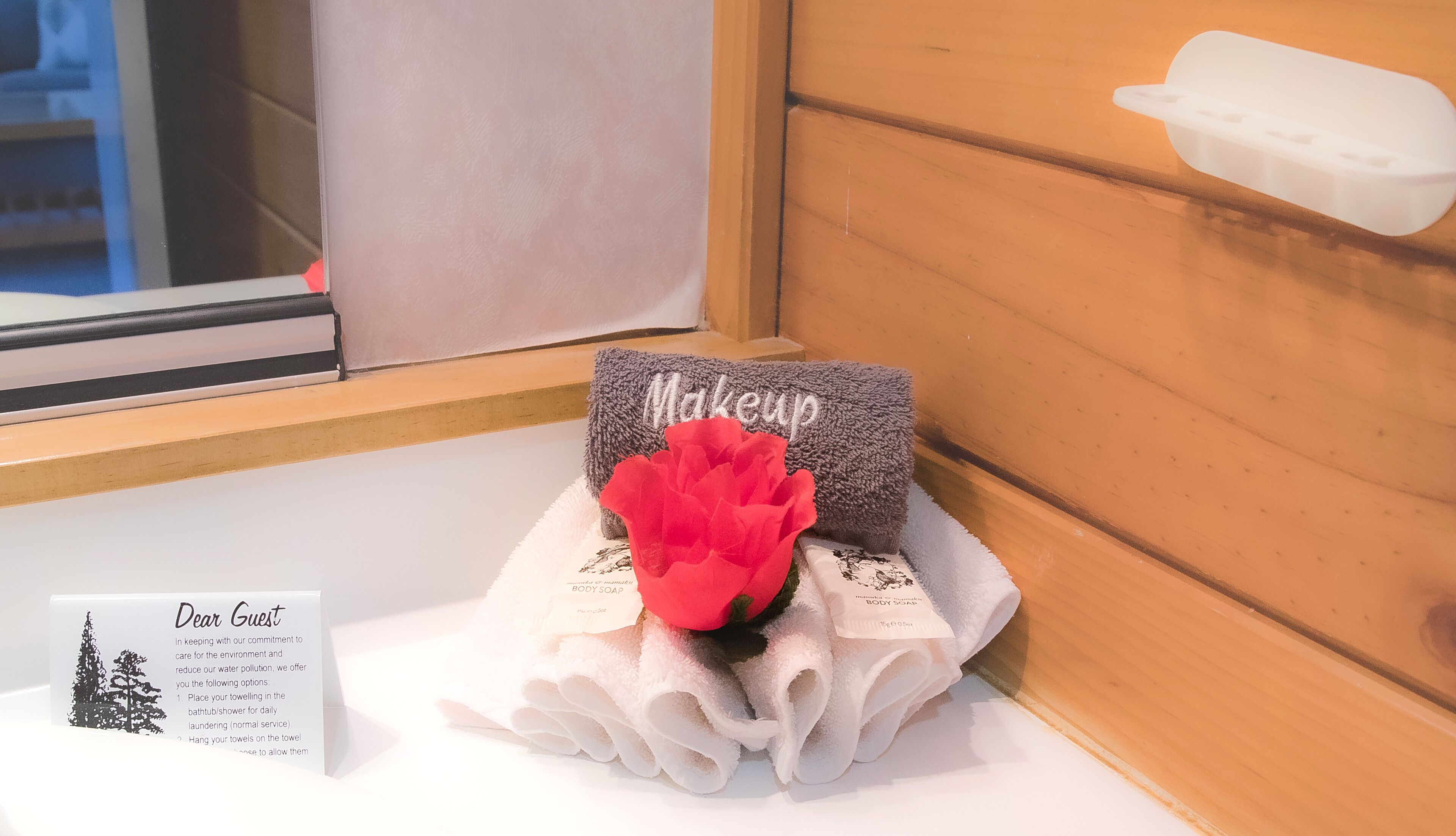 A bathroom with a window, a towel rack with a red flower, and a sign offering towel drying options.