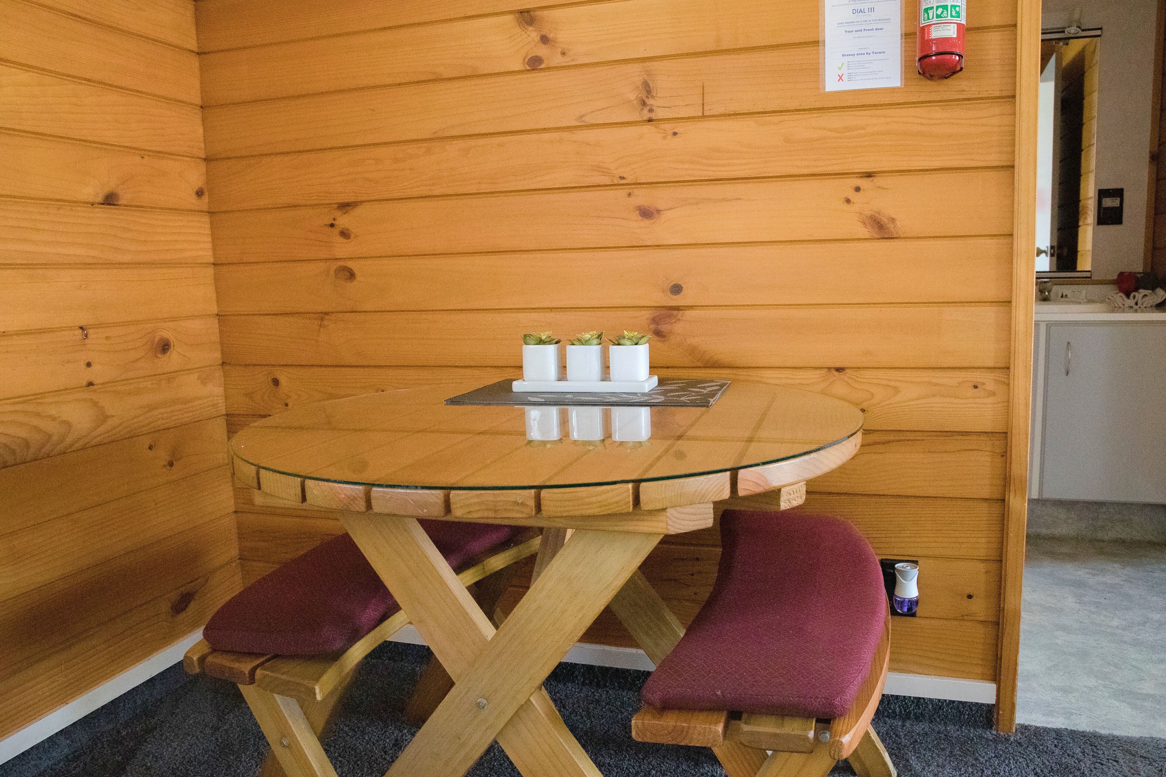 A small wooden room with a round glass table and two cushioned chairs.