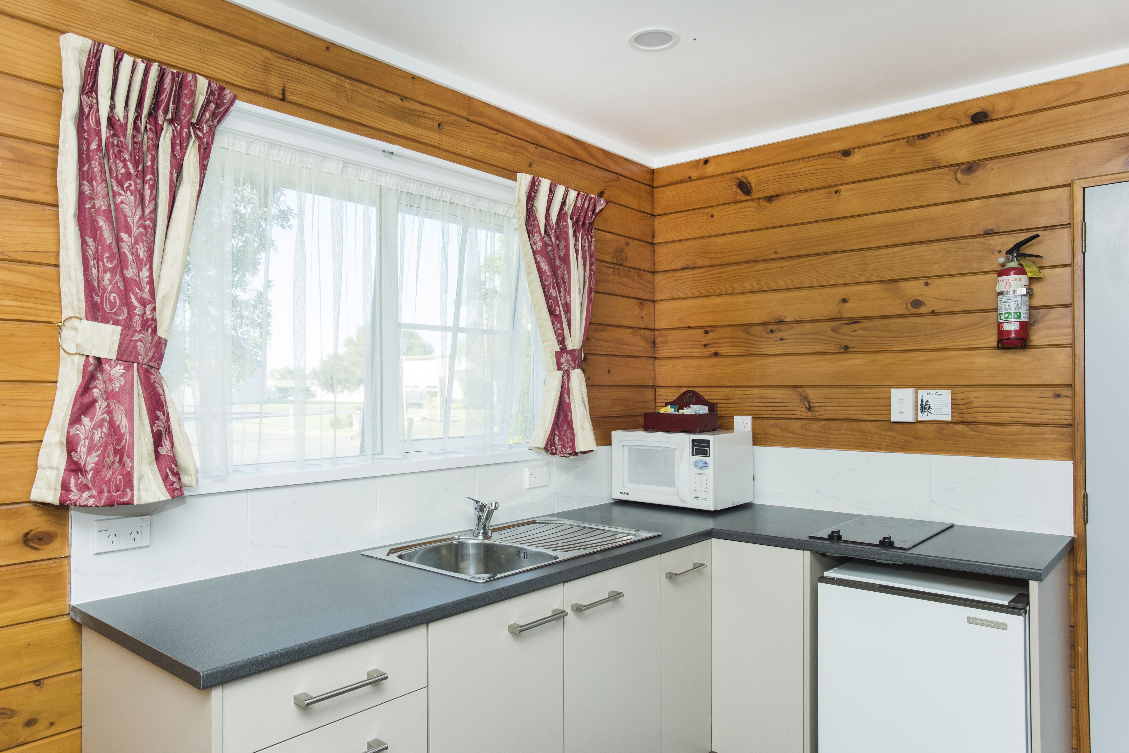 Una cocina funcional con paredes de madera, un lavamanos, un microondas y un lavavajillas.