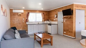 A compact living space with a kitchenette, a sofa, a coffee table, and a television mounted on the wall. - Tudor Park Motel (Gisborne)