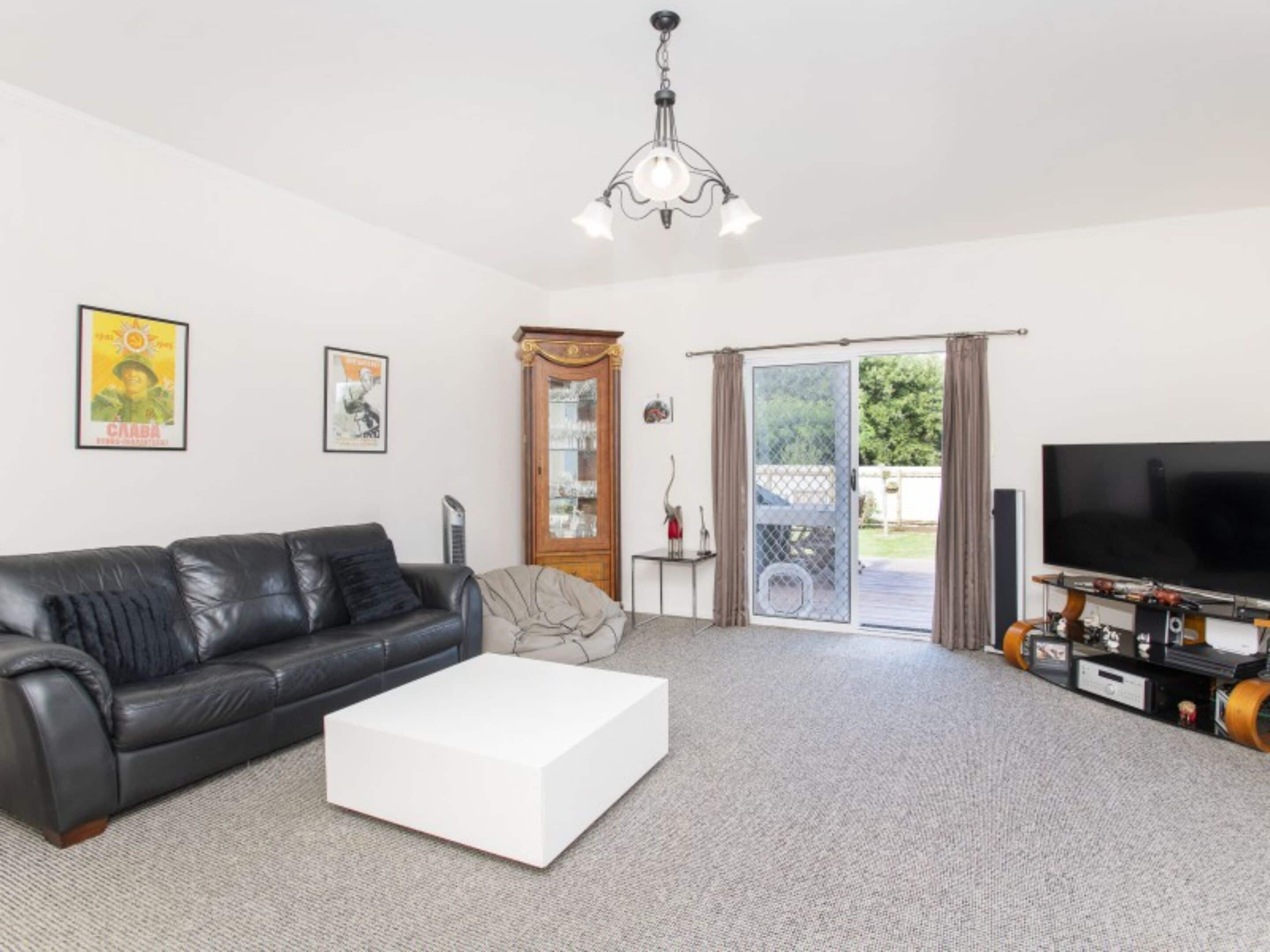 A living room with a black leather sofa, a white coffee table, a TV, and a chandelier.