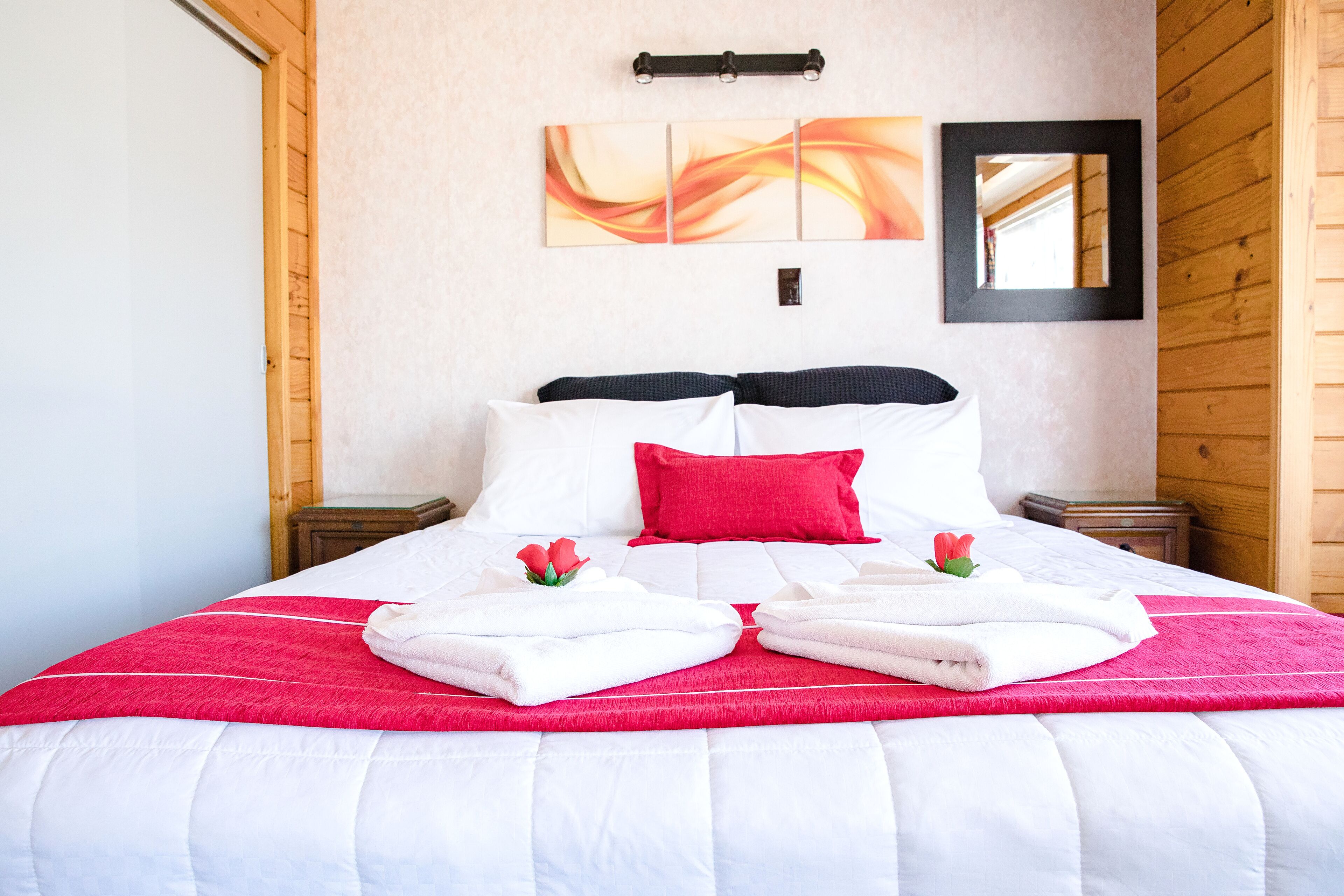 A neatly made bed with white and red bedding, a red pillow, and two towels folded on the bed.