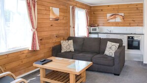 A cozy living room with a sofa, a coffee table, and a kitchen in the background. - Tudor Park Motel (Gisborne)