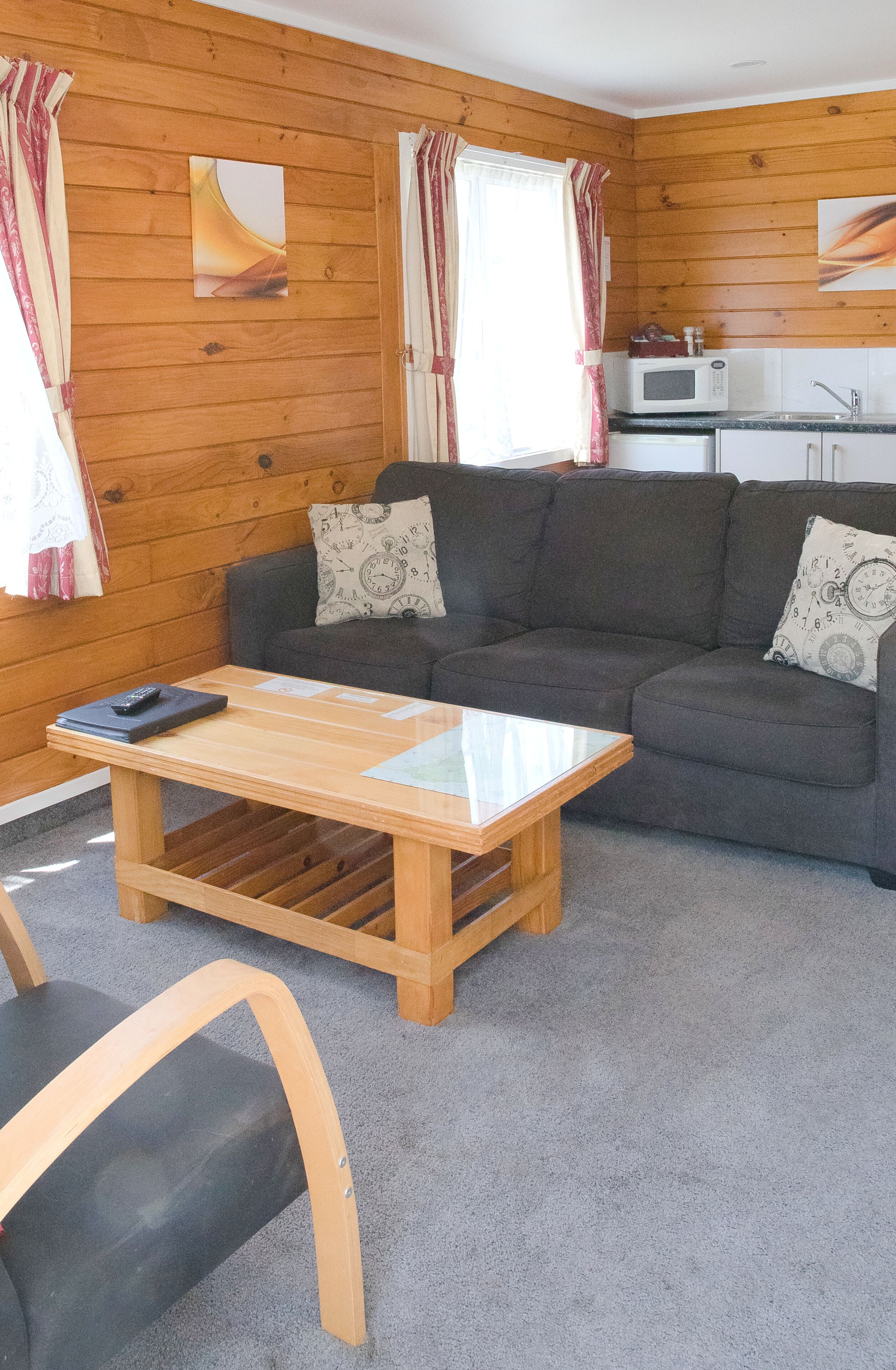 Una habitación acogedora con pared de madera, un sofá gris, una mesa de centro de madera y una pequeña cocina con microondas.