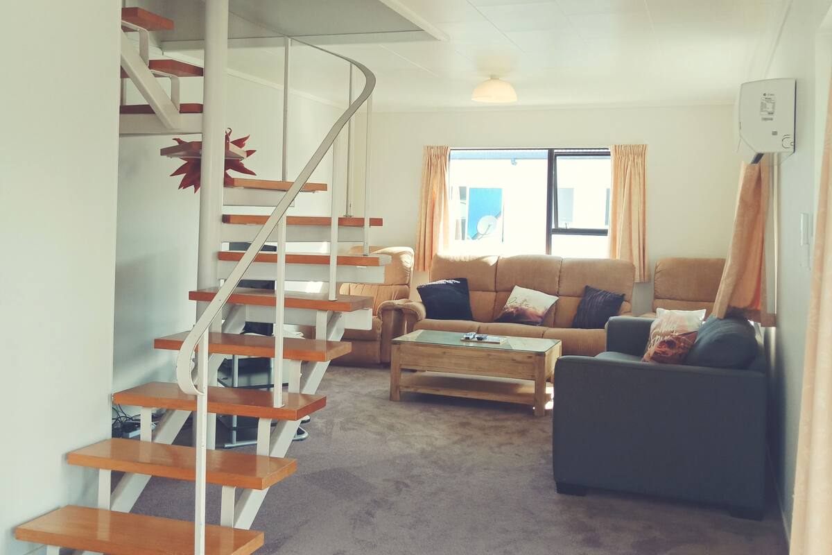 A living room with a wooden staircase, a sofa, a coffee table, and a window with curtains.