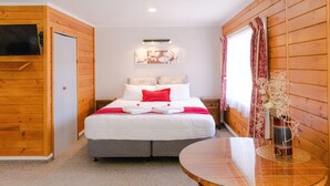 A hotel room with a bed, a TV, a table, and a window with curtains. - Tudor Park Motel (Gisborne)