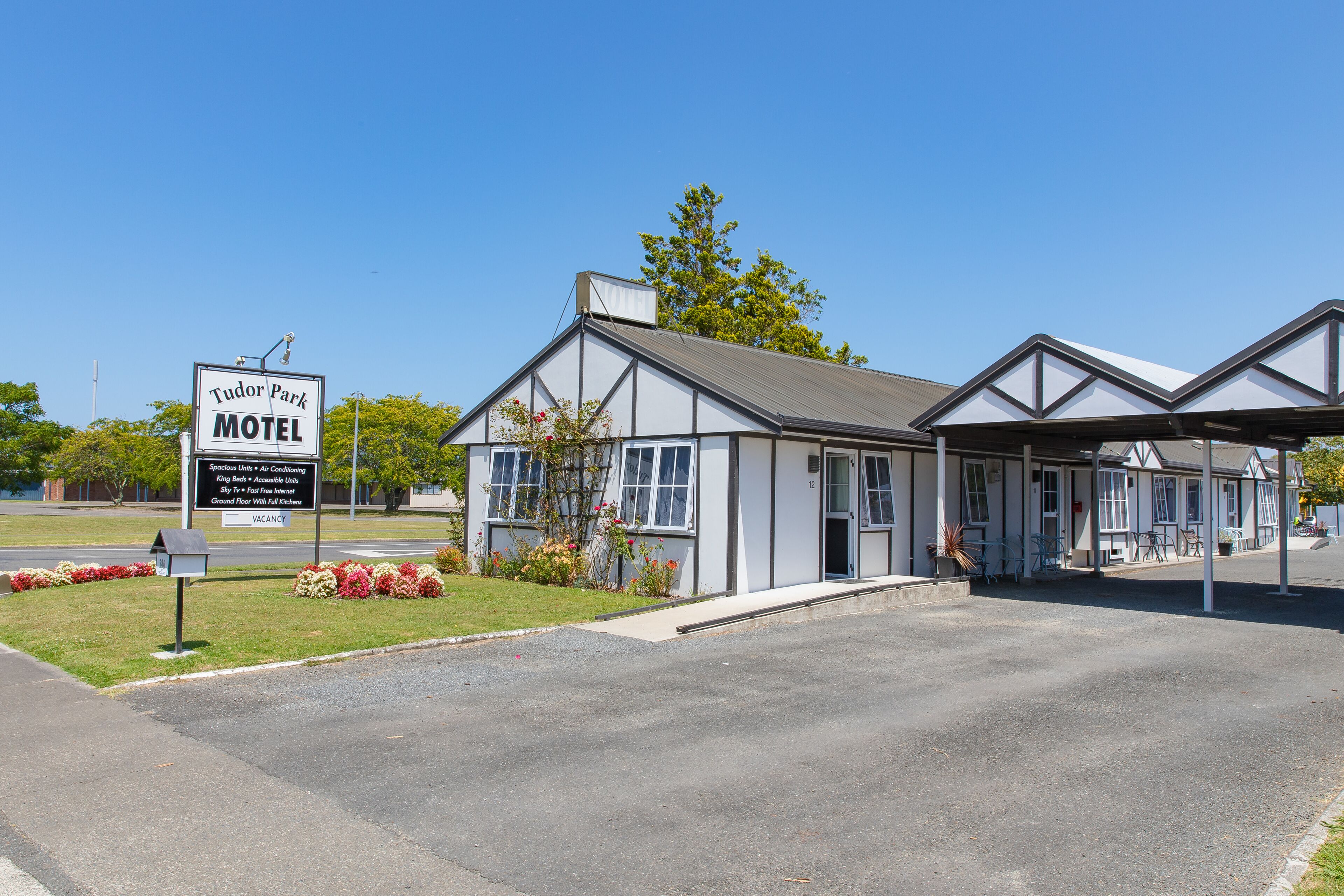 Un motel Tudor Park con un camino de acceso despejado, un cartel anunciando los servicios y un edificio sencillo de dos pisos con zona de estacionamiento techada.