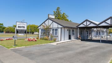 Un motel Tudor Park con un camino de acceso despejado, un cartel anunciando los servicios y un edificio sencillo de dos pisos con zona de estacionamiento techada.