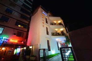 Een hotel met een neonreclame, een restaurant met een rode luifel, en een goed verlichte ingang.