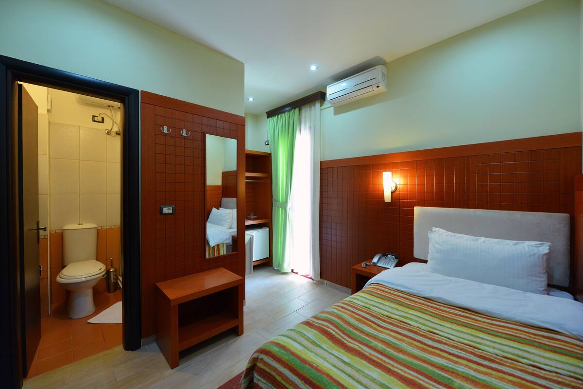 Une chambre d’hôtel avec un lit, une table de chevet et une salle de bain visible à travers une porte ouverte.