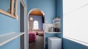 A compact room with a kitchenette, a small refrigerator, a sofa, and a window. - Victoria Railway Hotel (Invercargill)