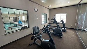 A fitness room with exercise equipment, a clock, and a view of an outdoor swimming pool. - Sleep Inn & Suites at Six Flags (San Antonio)