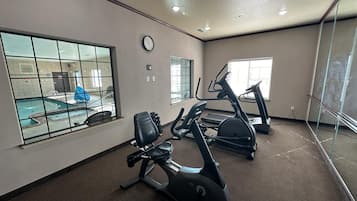 A fitness room with exercise equipment, a clock, and a view of an outdoor swimming pool.