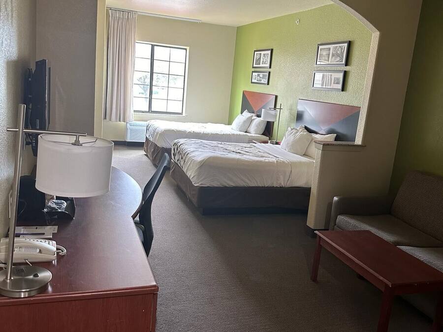 Quarto de hotel com duas camas, uma mesa com telefone, uma cadeira e uma pequena mesa.