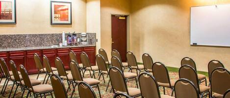 A conference room with rows of chairs, a whiteboard, and a kitchenette area.