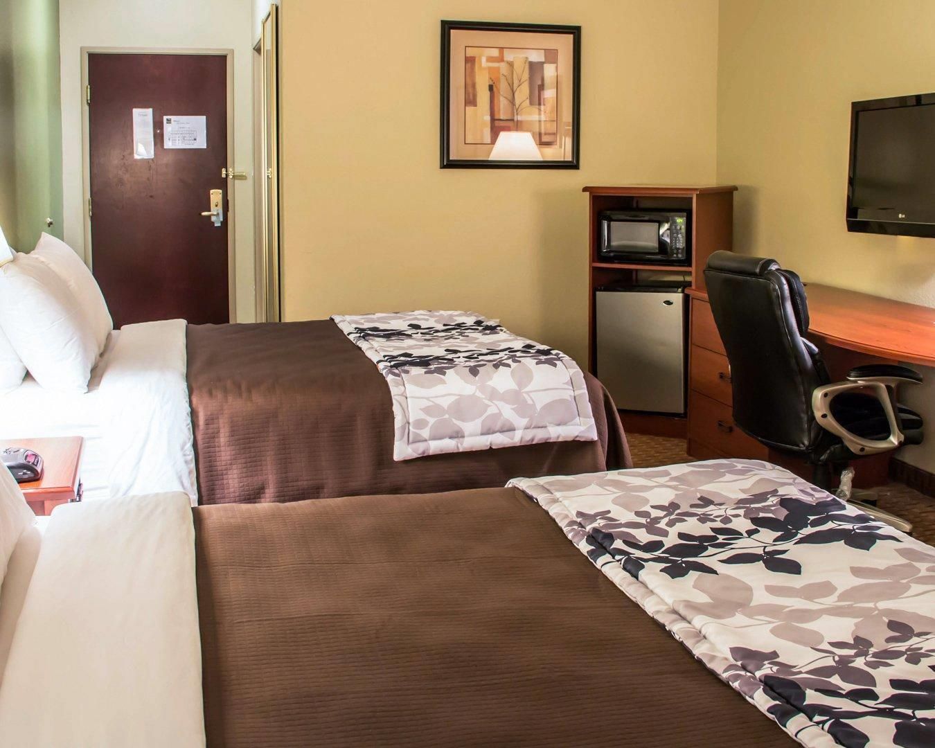 A hotel room with two beds, a desk, a chair, a television, and a refrigerator.