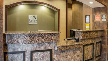 A reception desk with a sign for Sleep Inn & Suites, a computer, and a trash bin.