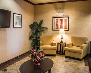 A hotel lobby with two armchairs, a table with a vase of flowers, a lamp, and framed artwork on the walls. - Sleep Inn & Suites at Six Flags (San Antonio)