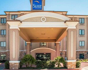 A Sleep Inn & Suites building with a central entrance, multiple windows, and a landscaped area with palm trees. - Sleep Inn & Suites at Six Flags (San Antonio)